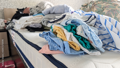 Close Up Of Messy Piles Of Colorful Clothing On Bed During Seasonal Wardrobe Decluttering