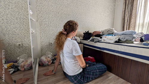 Obraz na płótnie Tired Young Woman Sorting Through Scattered Clothes During A Seasonal Wardrobe D