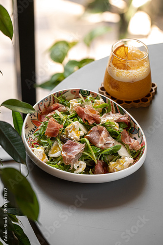 Fresh arugula salad with prosciutto slices and cheese served with a refreshing orange cocktail in a glass