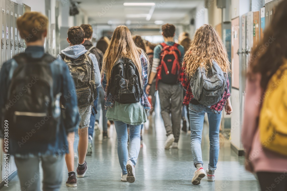 Fototapeta Students carrying backpacks walking along school hallway with students backpacks education teenagers corridor lifestyle learning academic together movement building interior schooling