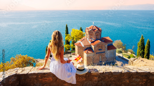 Fotografie Young woman in white dress holding macedonian flag looking at Saint John Kaneo c