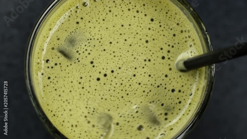 Refreshing matcha tea with ice cubes, stirring with black straw, close up