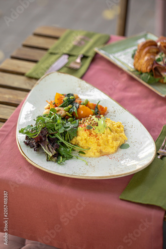 Healthy gourmet breakfast with scrambled eggs shrimps and fresh green salad served on pink tablecloth