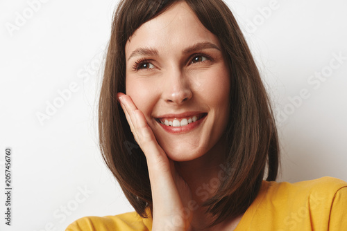 Foto A smiling brunette woman touches her cheek in a bright studio, implying confidence and a casual, everyday moment