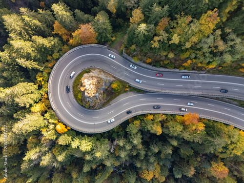 Aerial view of a hairpin mountain road curve with a cross on rock in autumn