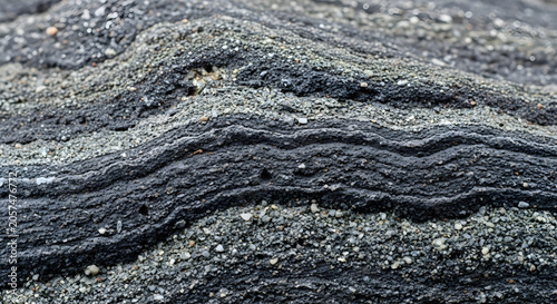 Natural geological texture with stratified dark and light grey rock layers and granular sand abstract background
