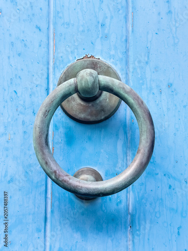 Obraz na plátně Old door knocker — close-up of a weathered bronze ring door knocker with green verdigris patina on a vivid blue painted wooden door wet from rain on Stromboli, Aeolian Archipelago, Sicily, Italy