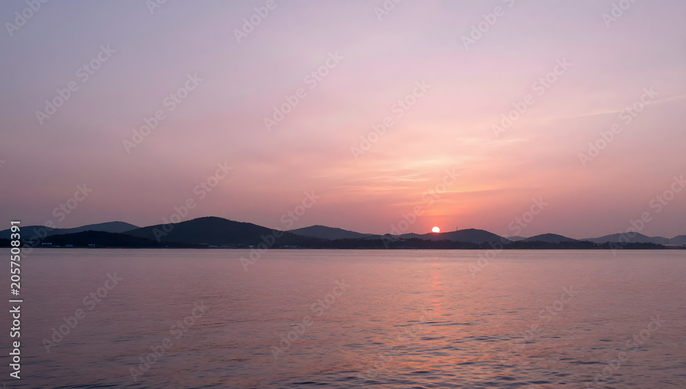 Fototapeta premium Serene Sunset Over Water: A breathtaking sunset paints the sky with hues of pink and orange, casting a soft glow over a calm body of water and a distant, silhouetted mountain range.