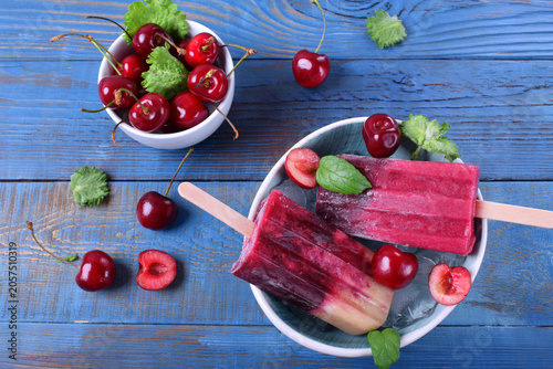 Fruit and berry popsicles, cherries and mint in a ceramic bowl against the blue background. Frozen dessert, top view