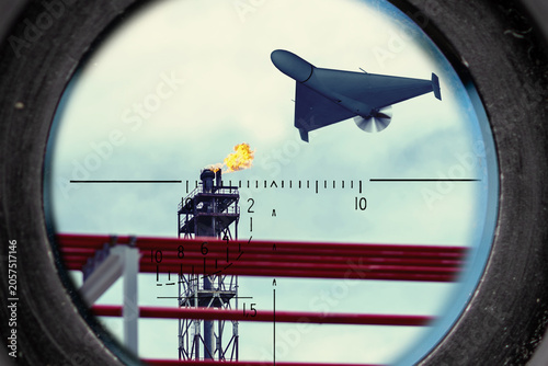 Strike drone flies above oil and gas facility with burning flare stack under surveillance.