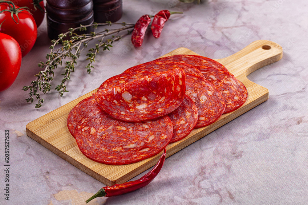 Obraz premium Spicy salami slices on wooden cutting board with fresh tomatoes and chili peppers