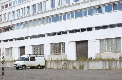 Tableau sur toile A lonely old rusty white minibus is parked near a white industrial building, Bad