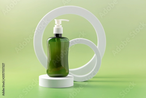 Bottle with pump dispenser standing on a white podium next to geometric shapes on a green background