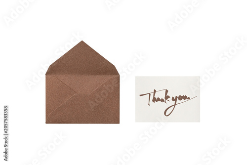 Overhead view of a cutout of a brown lamé envelope with a brown handwritten thank-you card placed next to it	