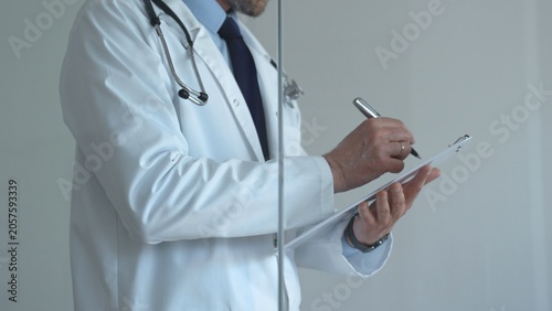 Schilderij op canvas Doctor working, making notes on a clipboard with a pen, wearing a white coat and