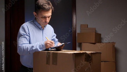 Cuadro en lienzo Man in a blue shirt standing beside stacked cardboard boxes, carefully checking