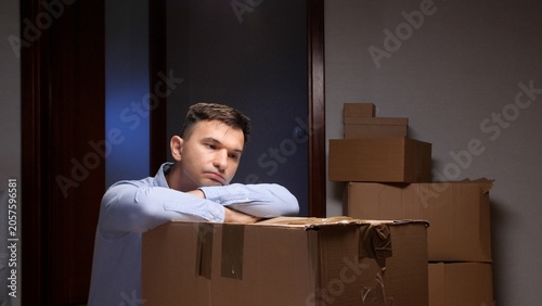 Foto Man resting head on cardboard box, expressing sadness and exhaustion amidst stac