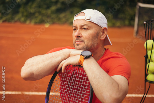Tennis coach holding a racket on a clay court, professional sports setting with focused confident posture, natural daylight