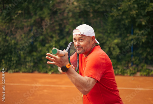 Tennis coach holding a racket on a clay court, professional sports setting with focused confident posture, natural daylight