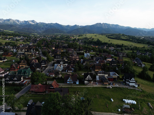 Panoramic aerial view of a scenic mountain village in Podhale with the majestic Tatra Mountains and Giewont peak in background, Poland.