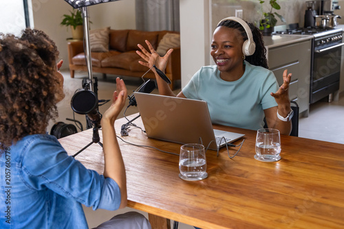 African American female co-hosts recording podcast at home studio with laptop, condenser mic