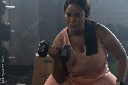 Foto African American woman performing bicep curl at gym holding hex dumbbell in pink