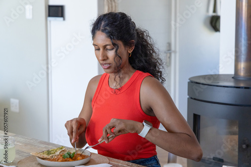 Asian woman in red top sitting at dining table cutting meal with fork and knife today