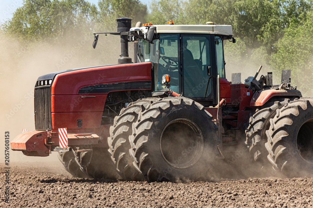Obraz premium Large powerful tractor working on agricultural field during spring sowing