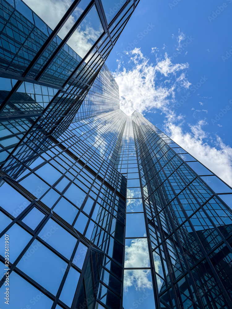 Obraz premium Glass skyscraper reflecting blue sky and clouds.