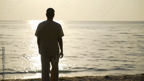A gender-neutral person in minimalist natural fabric clothing stands peacefully at the serene ocean edge, bathed in golden hour light with shimmering water and a softly blurred background. Profound