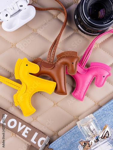 Fotografie Close-up of a leather bag charm featuring three horses — yellow, brown, and pink — on a beautiful table with women's items