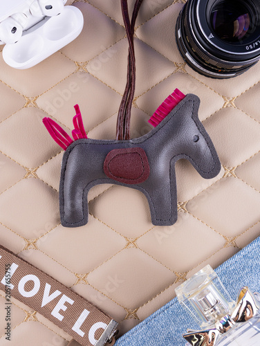 Photos Close-up of a leather bag charm featuring a gray horse with a pink mane, placed on a beautiful table with women's items
