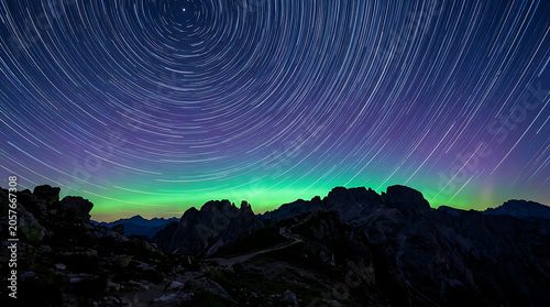 Celestial star trails over aurora borealis and rocky mountain peaks at night