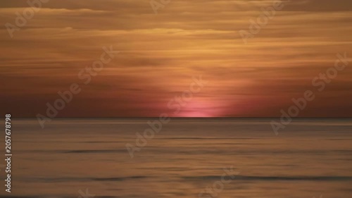 Cinematic time-lapse video of a breathtaking, hyper-realistic sunset over an expansive, calm ocean, with the sky transforming from golden hour to fiery oranges and deep purples, mirrored by the