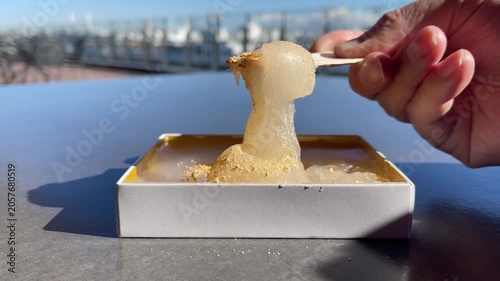 きな粉をトッピングした和菓子のわらび餅の動画。木製スプーンで食べようとしてる様子。