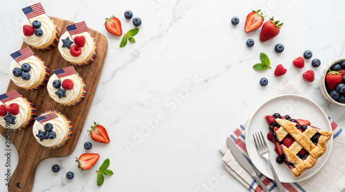 Patriotic cupcakes and berry pie slice for fourth of july celebration on white marble background with fresh fruit toppings