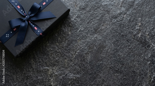Elegant black gift box with patriotic ribbon on dark stone background for independence day celebration