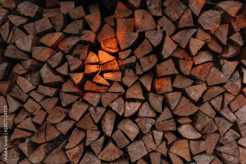 Beautifully stacked firewood glowing in warm sunset light. Cozy natural scene with golden reflections and soft evening atmosphere.