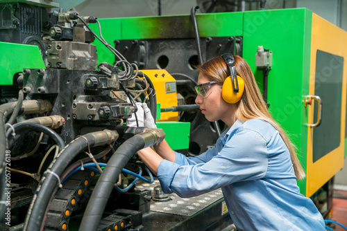 Принти на полотні Female factory worker inspecting industrial machinery, wearing safety gear