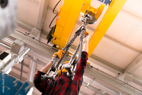 Принти на полотні The worker is wearing a hard hat and using a crane to lift a heavy load in a busy factory setting with various equipment and machinery visible in the background