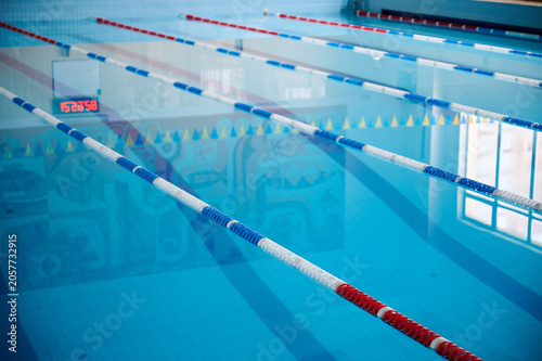 Indoor swimming pool lanes with calm blue water. Lane dividers and reflections with digital timer visible, clean sport facility background
