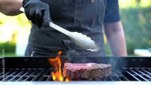 A professional chef's skilled hands meticulously turn a seared steak and premium ingredients on a sizzling barbecue grill, with dynamic flames, backlit smoke, and shallow depth of field, concept of