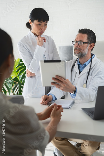 Medical specialists discussing treatment options with patient in clinic. Second opinion, collaborative healthcare and expert medical care concept