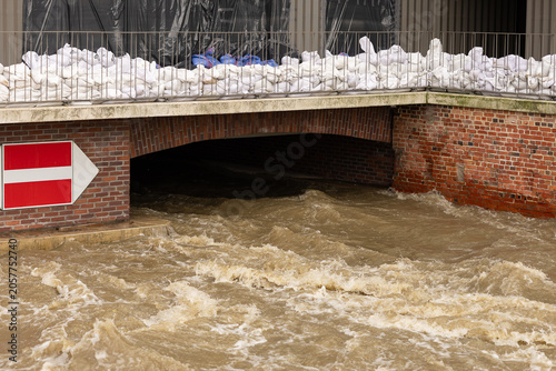 White sandbags protective barrier on a bridge railing over rushing muddy river water during city flood. Emergency natural disaster protection, high water control and defense