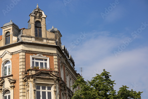 Photography Beautiful historic tenement house facade with ornate architectural details, windows, balcony, green tree and blue sky on sunny day