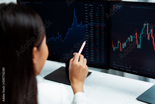 Εκτύπωση καμβά Young beautiful Asian businesswoman pointing with pen in exchange stock market on pc screen at back side view, analyzing profit at modern office, investing high profit valed in wealth