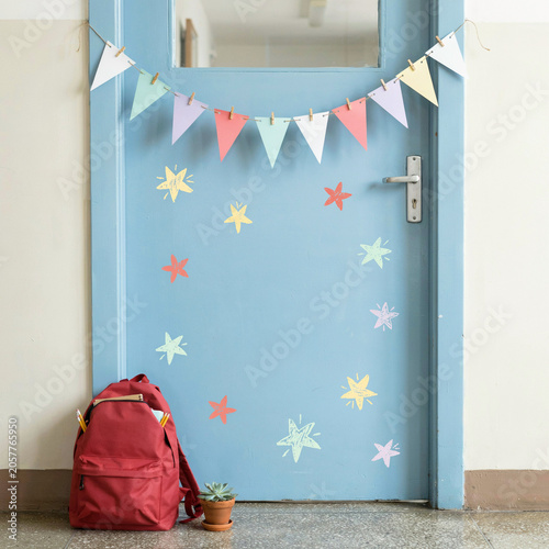 Backpack stands on the floor next to a blue door decorated with colorful star stickers and a festive paper bunting flag.