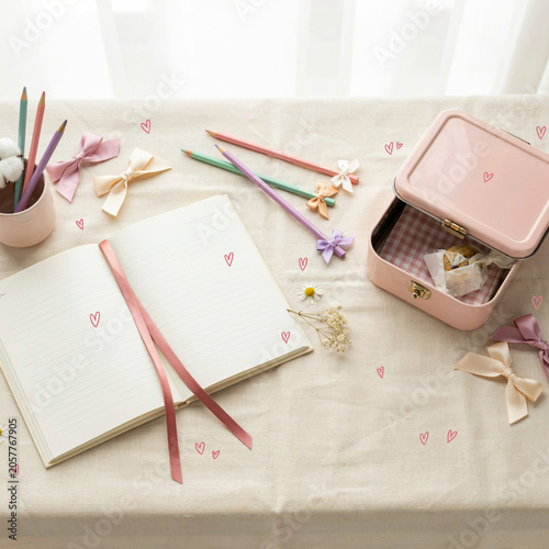 Diary with a pink ribbon bookmark lies on a table beside a storage container and decorative bow ornaments.