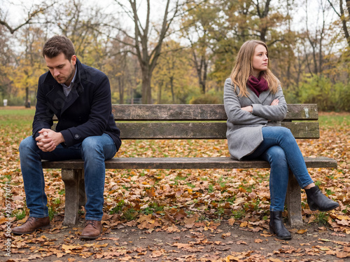 Unhappy couple sitting separated on a park bench, showing a breakup, conflict, and silent treatment in autumn