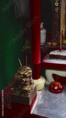 Minute movements of smoke coming from lit incense staked on a foo dog statue in an altar shrine depicting the rituals and offerings in Chinese Buddhism. Central, Hong Kong